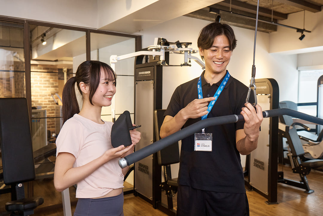 トレーニングマシンの使い方を教えてもらっている女性の画像